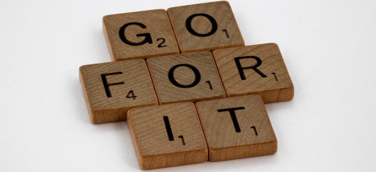 Close-up of Scrabble letters forming the phrase 'Go For It' on a white background.