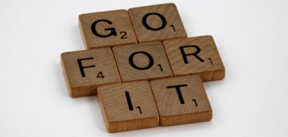 Close-up of Scrabble letters forming the phrase 'Go For It' on a white background.