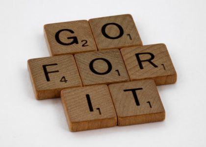 Close-up of Scrabble letters forming the phrase 'Go For It' on a white background.